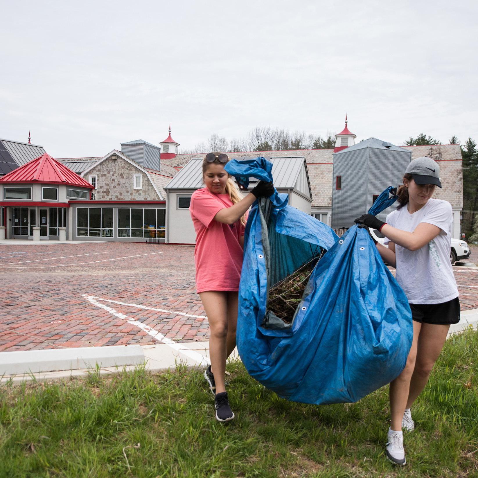 Two students carrying sticks and other debris on a tarp